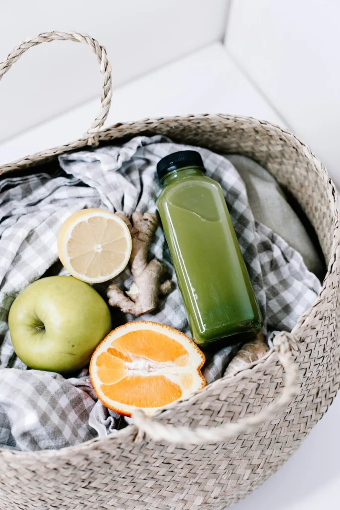 green bottle conainting vegetable juice beside orange fruit on brown woven basket